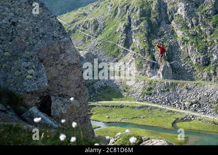 Lago Nero, Pinzolo, Italien - 2020. juli 18: Kleiner Junge mit rotem Hoodie und Hut üben Slackline an einem Seil zwischen zwei Gipfeln hängen, große Höhe a Stockfoto