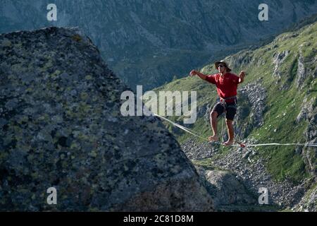 Lago Nero, Pinzolo, Italien - 2020. juli 18: Kleiner Junge mit rotem Hoodie und Hut üben Slackline an einem Seil zwischen zwei Gipfeln hängen, große Höhe a Stockfoto