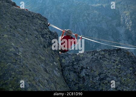 Lago Nero, Pinzolo, Italien - 2020. juli 18: Kleiner Junge mit rotem Hoodie und Hut üben Slackline an einem Seil zwischen zwei Gipfeln hängen, große Höhe a Stockfoto