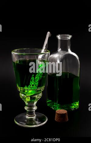 Alkoholisches Getränk, kreatives Stimulans und unkonventionelle Lifestyle-Konzept Thema mit Glas grünen Absinth und Edelstahl Löffel neben einem Vintage-Bott Stockfoto