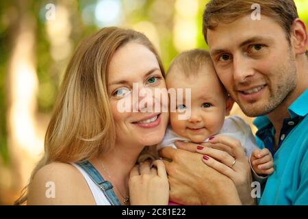 Glückliche Familie verbrachte Zeit zusammen im Freien. Porträt von Mutter, Vater und Baby beim Blick auf die Kamera. Sommerzeit. Stockfoto