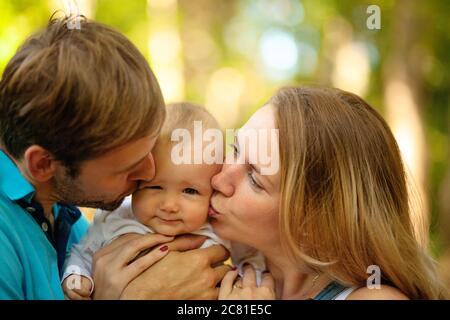Glückliche Familie verbrachte Zeit zusammen im Freien. Porträt von Mutter, Vater und Baby beim Blick auf die Kamera. Sommerzeit. Stockfoto