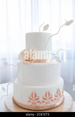 Elegante dreistufige Hochzeitstorte, mit königlichem Glasur bedeckt mit schönen Pfirsichfarben-Akzenten, essbaren Blumen und Details, Teil einer Backwerkstatt Stockfoto