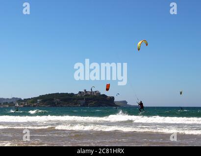 Kitesurfer oder Kiteboarder springen Kitesurfen vom Strand von Somo an einem sonnigen, windigen Nachmittag Santander Cantabria Spanien Sommer Stockfoto