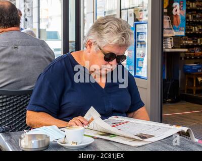 Ältere Frau beim Lesen der Zeitung am Café-Tisch - Frankreich. Stockfoto