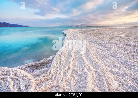 Morgensonne scheint auf Salzkristallen Formationen, klares cyangrünes ruhiges Wasser in der Nähe, typische Landschaft am ein Bokek Strand, Israel Stockfoto