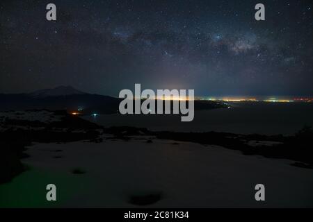 Nachthimmel mit der Milchstraße über dem llanquihue See, Stadtlichter und dem calbuco Vulkan im Hintergrund Stockfoto