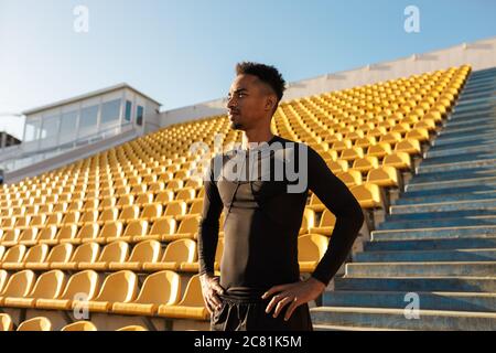 Der junge afroamerikanische Sportler blickt nachdenklich unter leeren Stadionsitzen weg Stockfoto