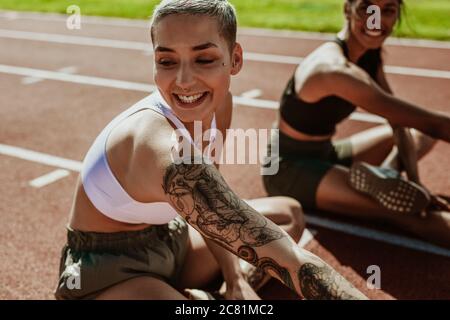 Läufer strecken sich die Beine und lächeln vor einem Streckenevent. Zwei junge Läufer üben im Leichtathletikstadion. Stockfoto