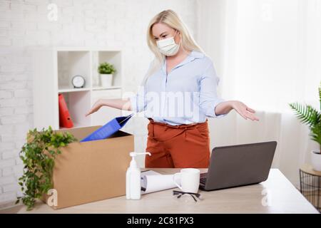 Business, Finanzkrise, Gesundheit, Sicherheit und Corona Virus Pandemie Konzept - Frau in Maske Verpackung Habseligkeiten nach ihrer Entlassung aus ihrer Arbeit Stockfoto