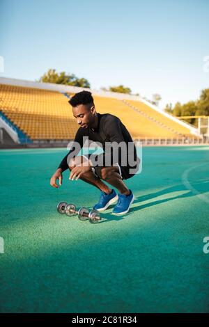 Junger afroamerikanischer Sportler, der mit Hanteln im Stadtstadion arbeitet Stockfoto