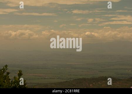 Landschaft umgeben von Bergen, die unter den flauschigen Wolken schimmern Stockfoto