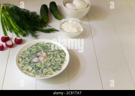 Kalte Suppe auf einem tiefweißen Teller mit Zutaten auf einem weißen Tisch. Okroshka, ein traditionelles Gericht der russischen Küche. Speicherplatz kopieren. Stockfoto