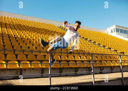 Junger selbstbewusster afroamerikanischer Sportler, der über den Zaun im Stadion springt Stockfoto