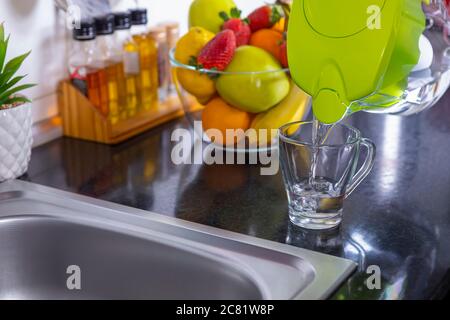 Aus der Wasserfilterkanne in der Küche gefiltertes Wasser in das Glas gießen. Reinigung und Enthärtung von Trinkwasser. Nahaufnahme. Konzentrieren Sie sich auf Glas. Stockfoto