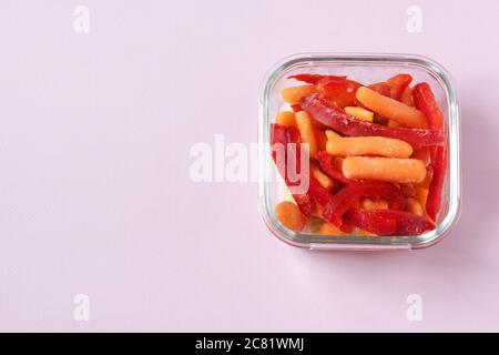 Gefrorenes Gemüse wie roter Paprika und Baby Karotte in den transparenten Schalen auf dem rosa Hintergrund mit Copyspace. Draufsicht. Stockfoto