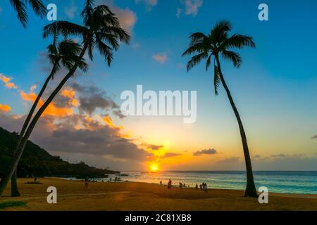 Touristen genießen den Strand am Waimea Bay Beach Park bei Sonnenuntergang; Oahu, Hawaii, Vereinigte Staaten von Amerika Stockfoto