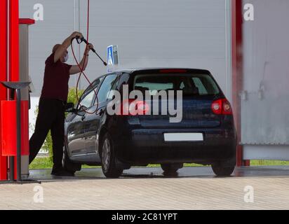 Ein Mann wäscht sein Auto mit einem Wasserdruckschlauch. Autoservice. Stockfoto