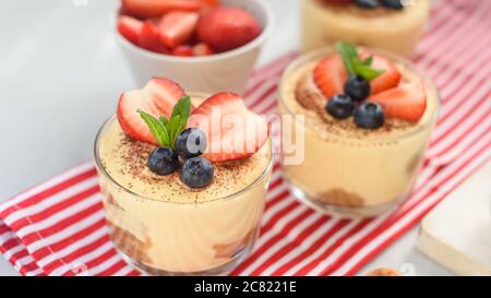 Hausgemachte, exquisite Dessert Tiramisu in Gläsern mit Erdbeere, Heidelbeere, Minze auf weißem Holztisch dekoriert, Draufsicht. Stockfoto