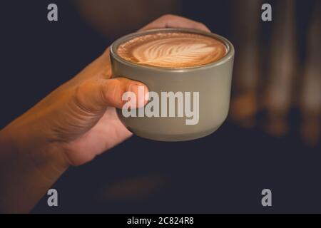 Hand hält eine Tasse Latte Kaffee Draufsicht zeigt Latte Kunst in Blattform Stockfoto