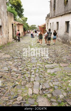 Colonia del Sacramento / Uruguay; 2. Januar 2019: Touristen, die in einem bewölkten Sommer eine gepflasterte Straße im historischen Zentrum der Stadt entlang gehen Stockfoto