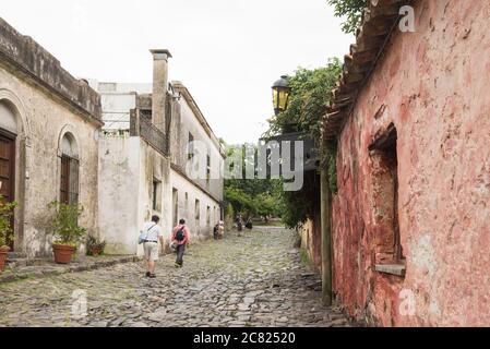 Colonia del Sacramento / Uruguay; 2. Januar 2019: Touristen, die in einem bewölkten Sommer eine gepflasterte Straße im historischen Zentrum der Stadt entlang gehen Stockfoto