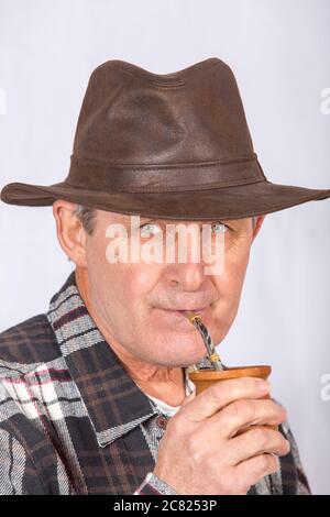 Attraktiver alter Mann mit klaren Augen und ländlichem Stil, der den typischen Aufguss in Argentinien und Uruguay namens Mate trinkt Stockfoto