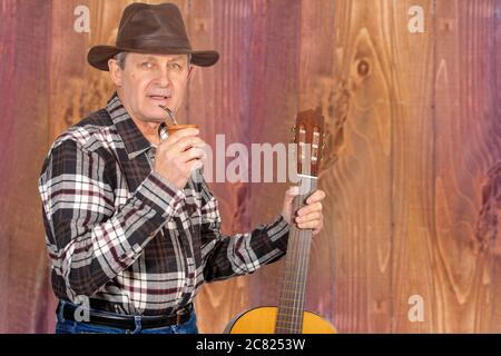 Attraktiver alter Mann mit klaren Augen und ländlichem Stil, der den typischen Aufguss in Argentinien und Uruguay namens Mate trinkt Stockfoto