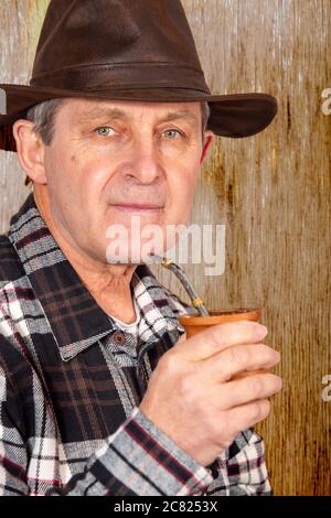 Attraktiver alter Mann mit klaren Augen und ländlichem Stil, der den typischen Aufguss in Argentinien und Uruguay namens Mate trinkt Stockfoto