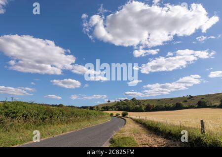 Ruhige Landstraße durch Ackerland im Meon Valley. Ein perfekter Sommertag, um auf dem Land mit blauem Himmel und weißen Wolken zu sein. Stockfoto