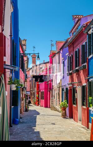 Burano Insel schmale gepflasterte Straße zwischen bunten Häusern Gebäude mit bunten Wänden und Kleidung hängen an Wäscheleine, vertikale Ansicht, Provinz Venedig, Region Venetien, Norditalien Stockfoto