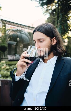 Junge gut aussehende nachdenkliche Brünette bärtigen Mann Wein im Restaurant im Freien trinken nachdenklich Stockfoto