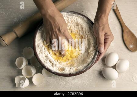Nahaufnahme von knienden Händen in einer Holzschale mit Mehl und Eier Backstock und Holzlöffel Stockfoto