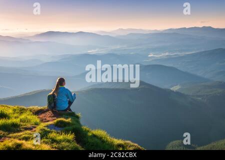 Frau mit Rucksack sitzt auf dem Berggipfel bei Sonnenuntergang Stockfoto
