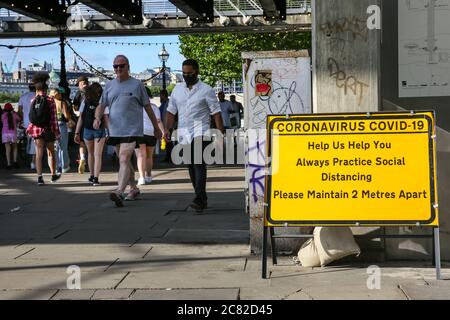 London, Großbritannien. Juli 2020. Gruppen von Menschen gehen an einem sozialen distanzierenden Erinnerungszeichen in der South Bank vorbei. An vielen öffentlichen Orten in London gibt es Schilder, die sich auf 2 Meter Entfernung halten, aber die Regeln werden nicht immer eingehalten, da viele Menschen die Entspannung der Absperrung und Geselligkeit bei warmem Wetter genießen. Kredit: Imageplotter/Alamy Live Nachrichten Stockfoto