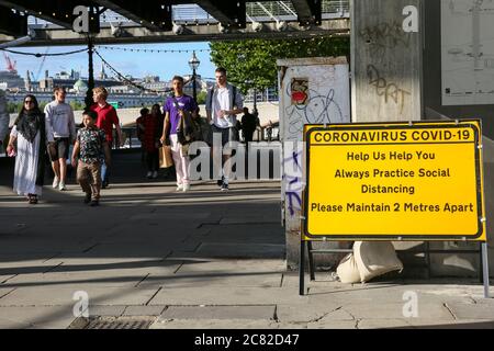 London, Großbritannien. Juli 2020. Gruppen von Menschen gehen an einem sozialen distanzierenden Erinnerungszeichen in der South Bank vorbei. An vielen öffentlichen Orten in London gibt es Schilder, die sich auf 2 Meter Entfernung halten, aber die Regeln werden nicht immer eingehalten, da viele Menschen die Entspannung der Absperrung und Geselligkeit bei warmem Wetter genießen. Kredit: Imageplotter/Alamy Live Nachrichten Stockfoto