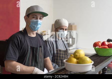 Hispanische Köche kochen in der Küche mit schützendem medizinischen Gesicht Masken Stockfoto
