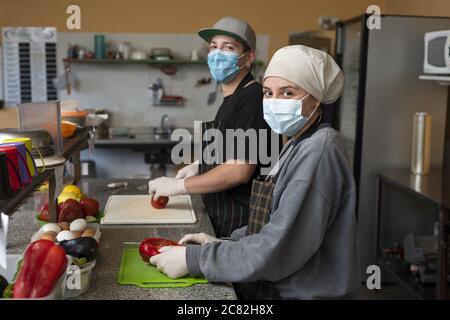 Hispanische Köche kochen in der Küche mit schützendem medizinischen Gesicht Masken Stockfoto