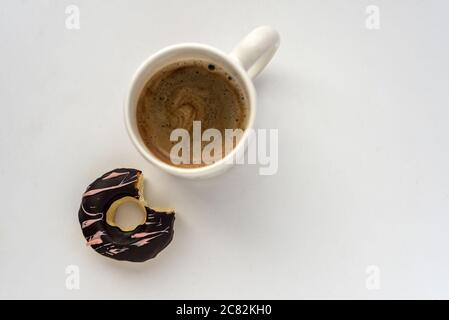 Overhead Schuss von einem leckeren Donut mit einer Tasse Kaffee auf einer weißen Oberfläche Stockfoto