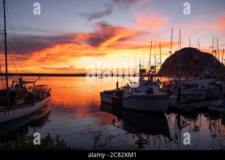Feurig rosa Himmel bei Sonnenuntergang über Morro Bay Marina mit Fischerbooten in ruhigem Wasser Stockfoto