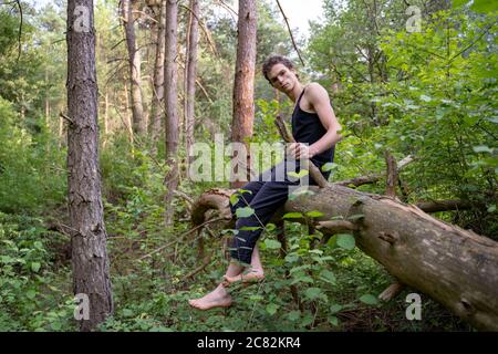 Seitenansicht Porträt des Mannes auf Holz sitzen gegen Bäume im Wald Stockfoto