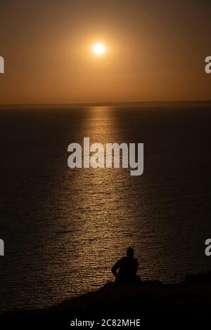 Portland, England. Juli 2020. Silhouette eines Mannes, der die untergehende Sonne über West Bay auf der Isle of Portland in England beobachtet. Die Insel Portand liegt in der Grafschaft Dorset. (Foto von Sam Mellish / Alamy Live News) Stockfoto