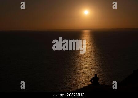 Portland, England. Juli 2020. Silhouette eines Mannes, der die untergehende Sonne über West Bay auf der Isle of Portland in England beobachtet. Die Insel Portand liegt in der Grafschaft Dorset. (Foto von Sam Mellish / Alamy Live News) Stockfoto