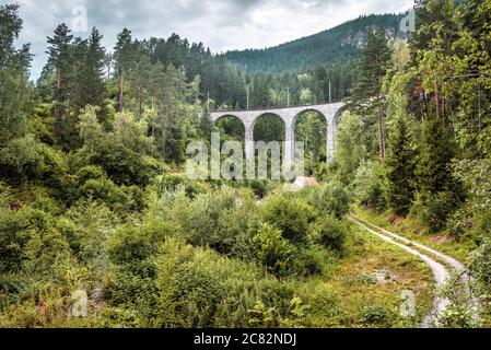 Landschaft mit altem Viadukt, Filisur, Schweiz. Landschaftlich schöner Blick auf die hohe Eisenbahnbrücke in den Alpen. Landschaft von grünen Wald und Landstraße, schöne Schweizer Stockfoto