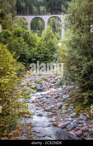 Landschaft mit altem Viadukt im Wald, Filisur, Schweiz. Landschaftlich schöne vertikale Ansicht der hohen Eisenbahnbrücke und felsigen Bach in den Alpen. Wunderschöne Schweizer Natur Stockfoto
