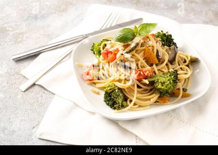 Vegetarische Spaghetti mit Brokkoli, Tomaten, Paprika und Auberginen, gesunde mediterrane Pasta-Mahlzeit auf einem weißen Teller und ein leichter rustikaler Backgroun Stockfoto