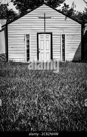 Ein grasbewachsener Vordergrund, eine gefälschte Kirche in Fake Town, einem von Mayberry inspirierten Kunstinstallationskomplex, im ländlichen mittleren Tennessee, USA, in Schwarz-Weiß Stockfoto