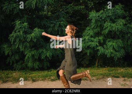 Frau läuft auf einem Feldweg in der Nähe der Bäume in Ein Kleid und Stiefel Stockfoto