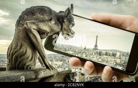 Gargoyle auf Kathedrale Notre Dame de Paris sieht Eiffelturm in Handy oder Handy, Paris, Frankreich. Lustige Foto von alten Paris und Smartphone. Co Stockfoto