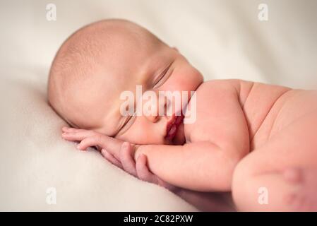Vorderansicht des neugeborenen Babys, das mit den Händen unter seinem schläft Kopf Stockfoto
